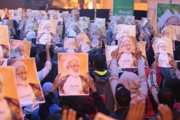 Sitters holding photos of Ayatollah Issa Qassim outside his residence in Diraz